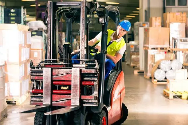 forklift driver in protective vest driving forklift at warehouse of freight forwarding company