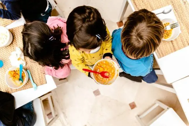 Girl walking with a bowl of stew in the dining room of her nursery school, top view, with copy space.