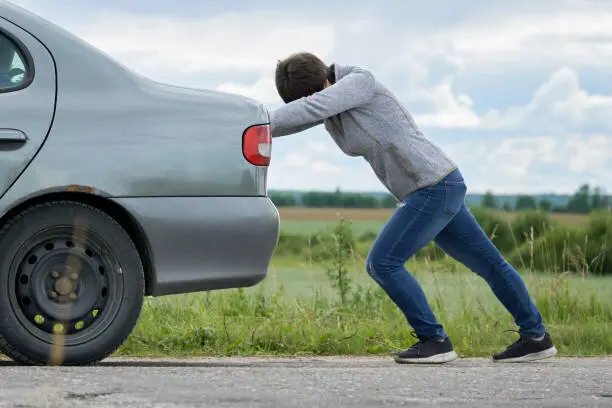Una persona empuja su coche averiado.