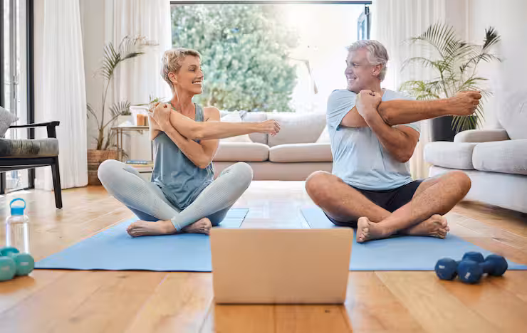 Pareja de personas de avanzada edad realizando ejercicios en casa.