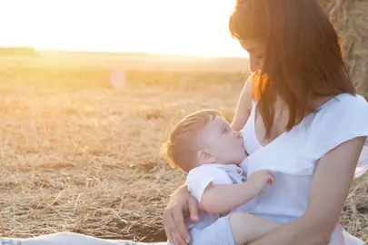 Beautiful happy mother breastfeeding her baby boy outdoor. Mother breastfeeding in a field at sunset in nature. Healthy eating.