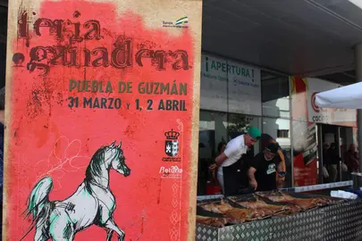 Cartel de la Feria y, al fonso, un asado del producto estrella, el cordero en extensivo