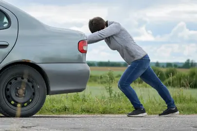 Una persona empuja su coche averiado.