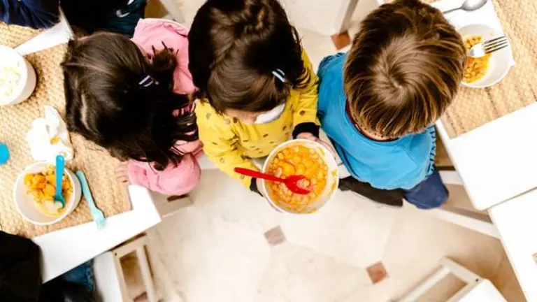 Girl walking with a bowl of stew in the dining room of her nursery school, top view, with copy space.