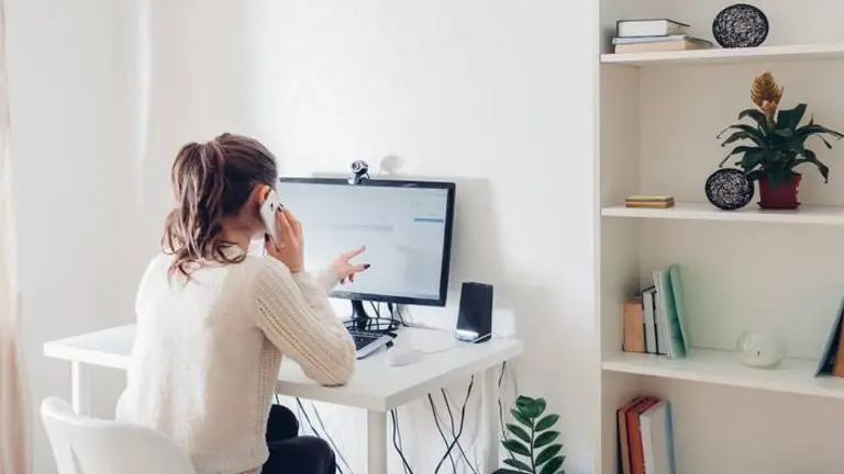 Work from home during coromavirus pandemic. Woman stays home talking on phone. Workspace of freelancer. Office interior with computer