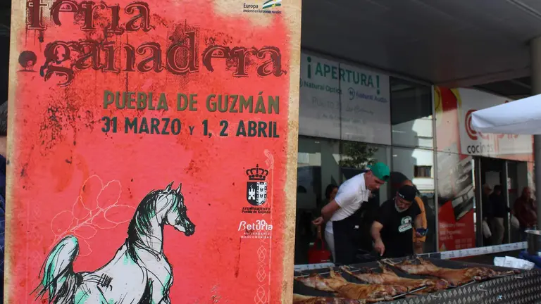 Cartel de la Feria y, al fonso, un asado del producto estrella, el cordero en extensivo