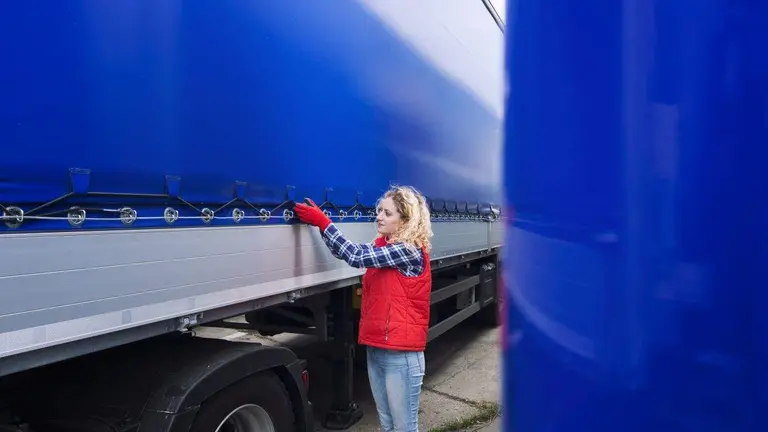 Female truck driver checking vehicle and tightening truck tarpaulin.
