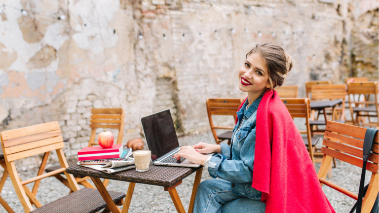Joven empresaria trabajando en el nuevo proyecto usando una computadora port&aacute;til durante la hora del almuerzo en la cafeter&iacute;a al aire libre.