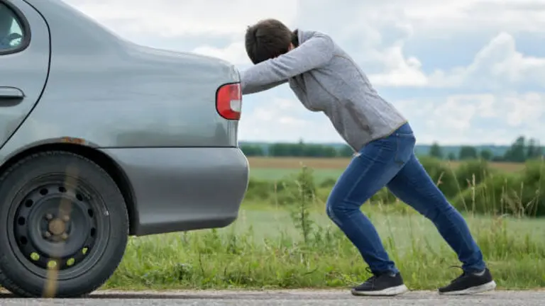 Una persona empuja su coche averiado.