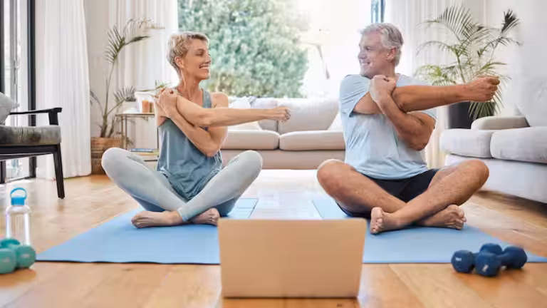 Pareja de personas de avanzada edad realizando ejercicios en casa.
